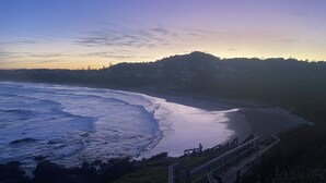 A coastal beach with waves, a wooden walkway, and a distant hill with buildings. - Spacious 4BR w/ Water Views (Port Macquarie)