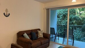 A living room with a brown sofa, two pillows, a small round table, and a view of a balcony with chairs. - Great Apartment Punta Esmeralda (Puntarenas Province)