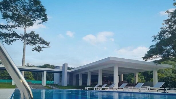 A swimming pool with lounge chairs and a covered area, surrounded by trees and greenery. - Great Apartment Punta Esmeralda (Puntarenas Province)