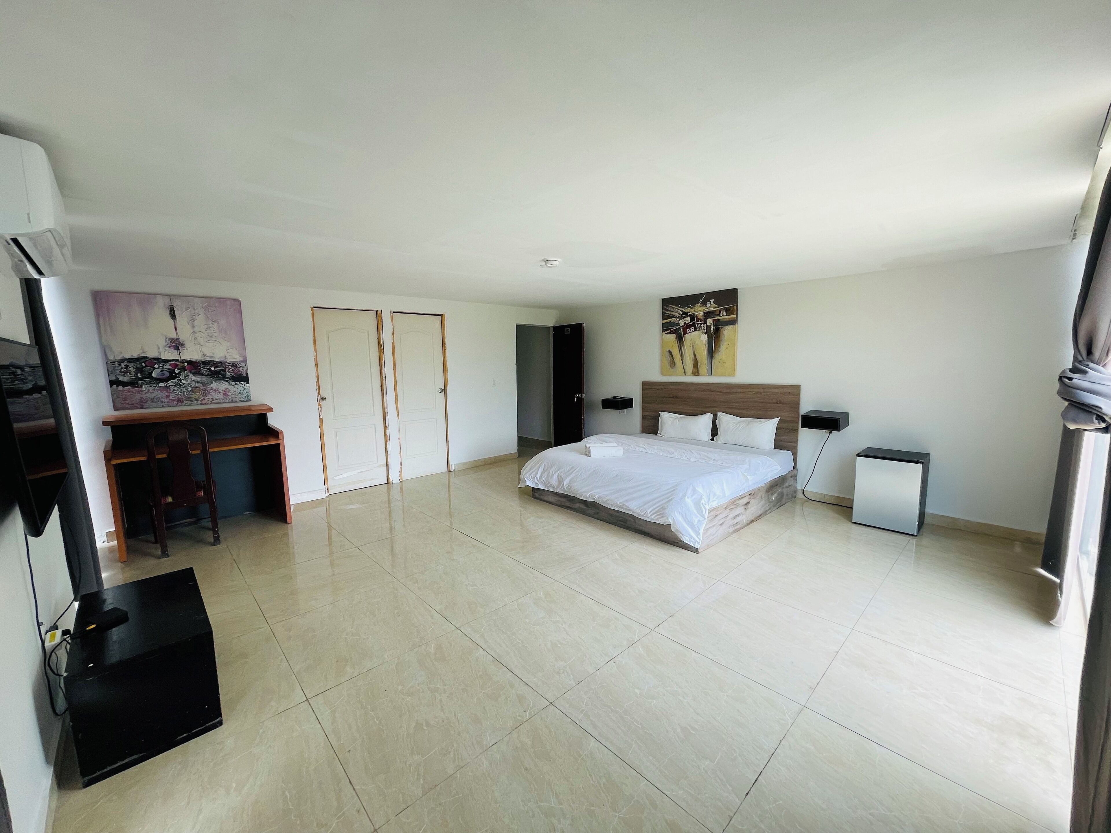 Un dormitorio amplio con una cama grande, un escritorio y una silla. Hay dos puertas y un cuadro en la pared.