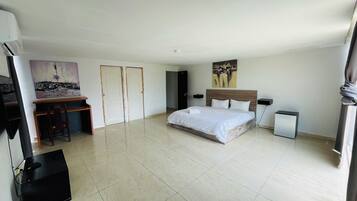 Un dormitorio amplio con una cama grande, un escritorio y una silla. Hay dos puertas y un cuadro en la pared.