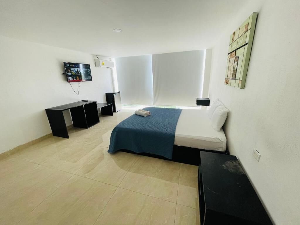 Un dormitorio con cama, escritorio, televisor y ventana.
