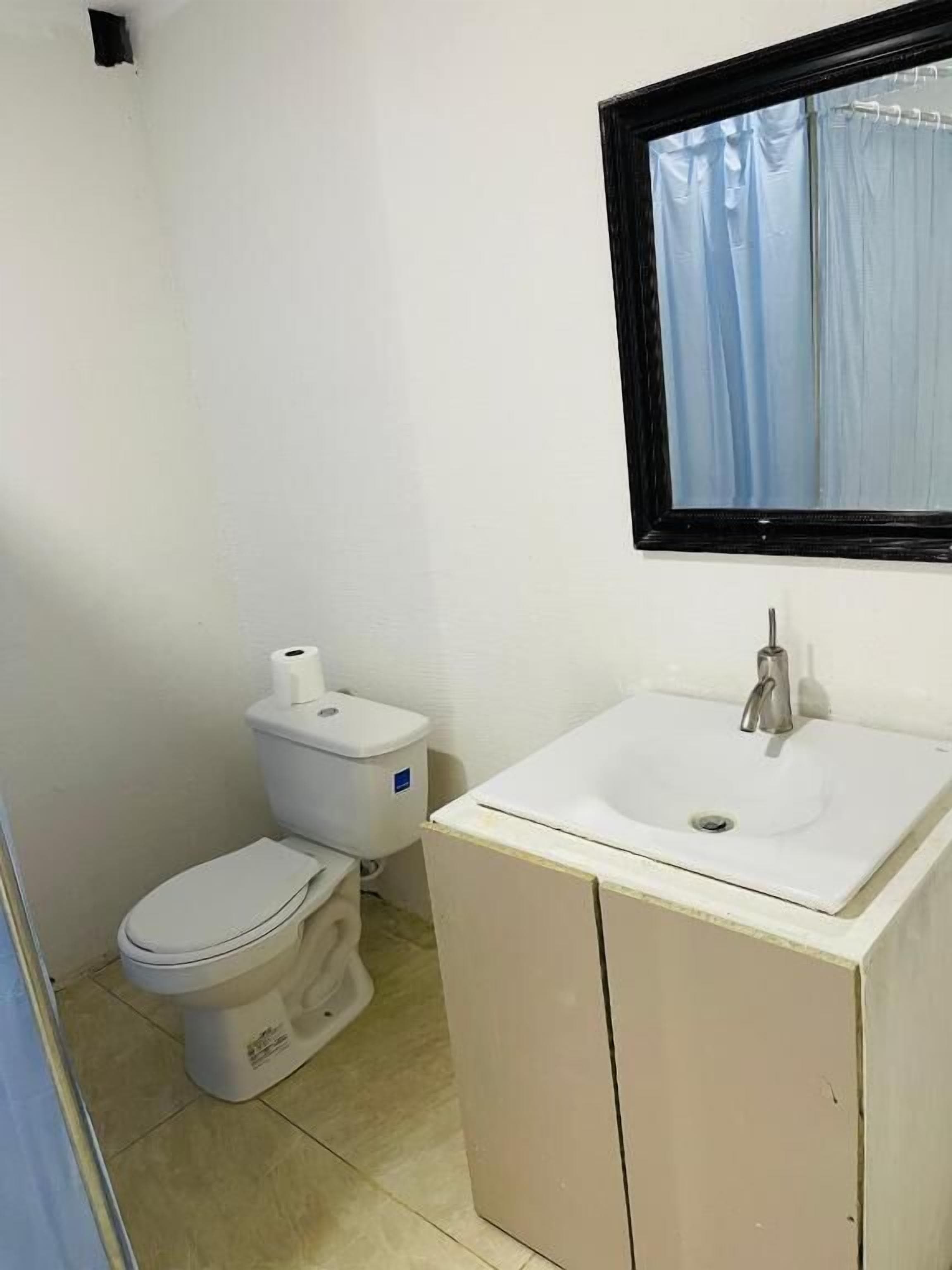 A small, clean bathroom with a toilet, sink, and a window with curtains.