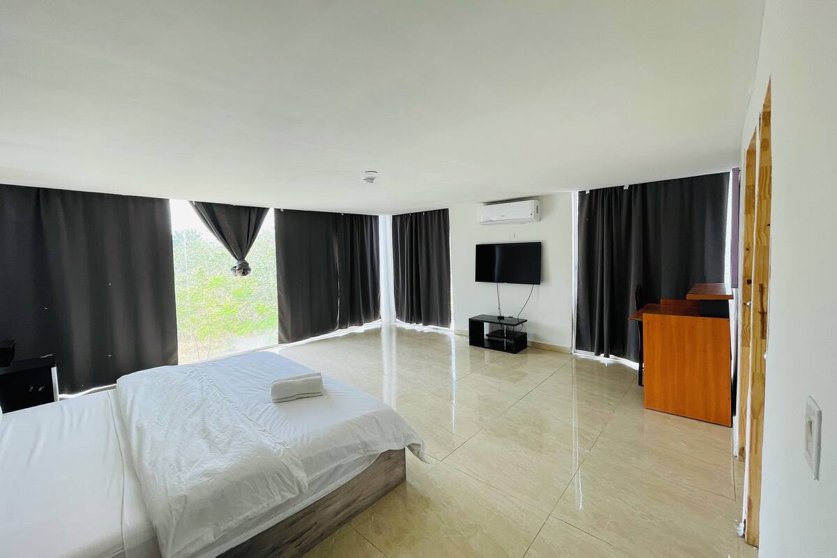 A hotel room with a bed, a TV mounted on the wall, a desk, and a window with curtains.