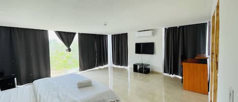 Ein Hotelzimmer mit einem Bett, einem an der Wand montierten Fernseher, einem Schreibtisch und einem Fenster mit Vorhängen.