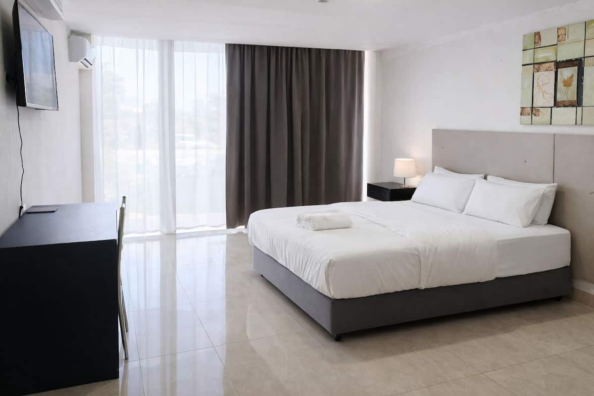 A hotel room with a bed, a desk, a chair, a TV, a lamp, and a window with curtains.