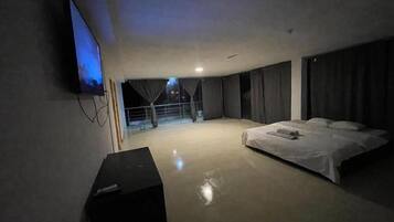 Ein Hotelzimmer mit einem großen Bett, einem an der Wand befestigten Fernseher und einem Balkon mit Vorhängen.