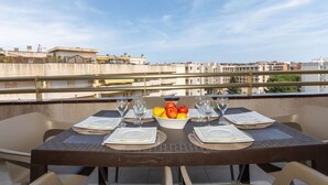 Une table à manger dressée pour quatre personnes, avec un saladier de fruits et des verres à vin, donnant sur un panorama urbain.