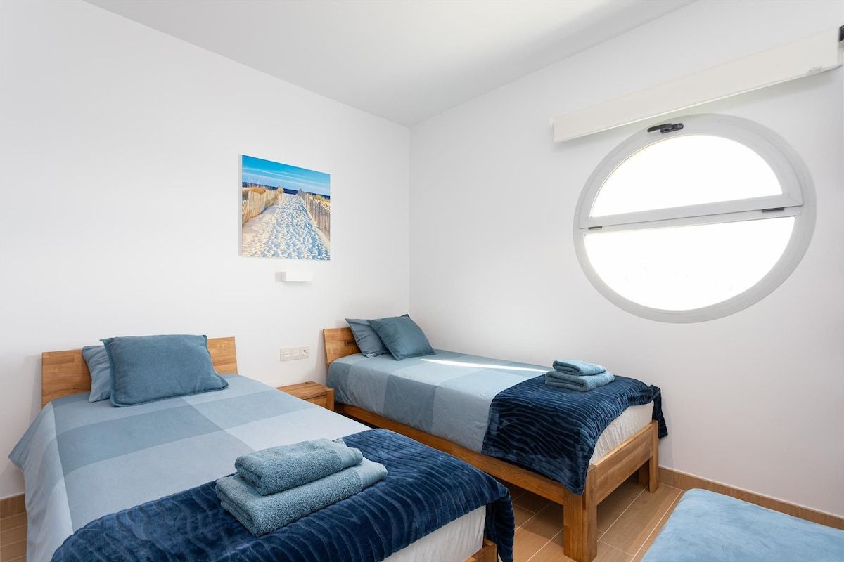 Ein Zimmer mit zwei Betten, einem Rundfenster und einer Wand-Klimaanlage.