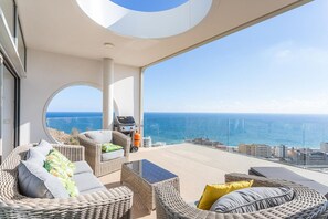 A balcony with wicker furniture, a grill, and a view of the ocean.
