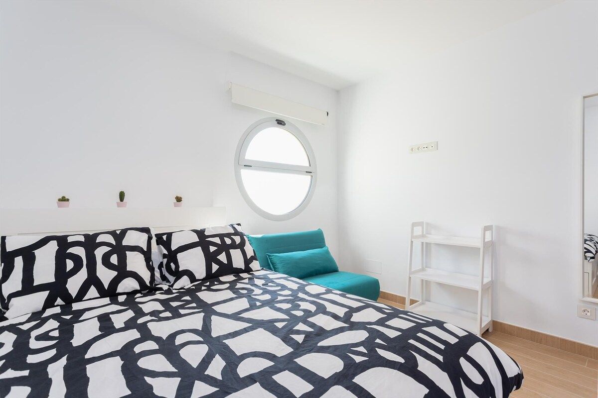 Een slaapkamer met een bed, een raam, een wit plankensysteem en een witte muur.