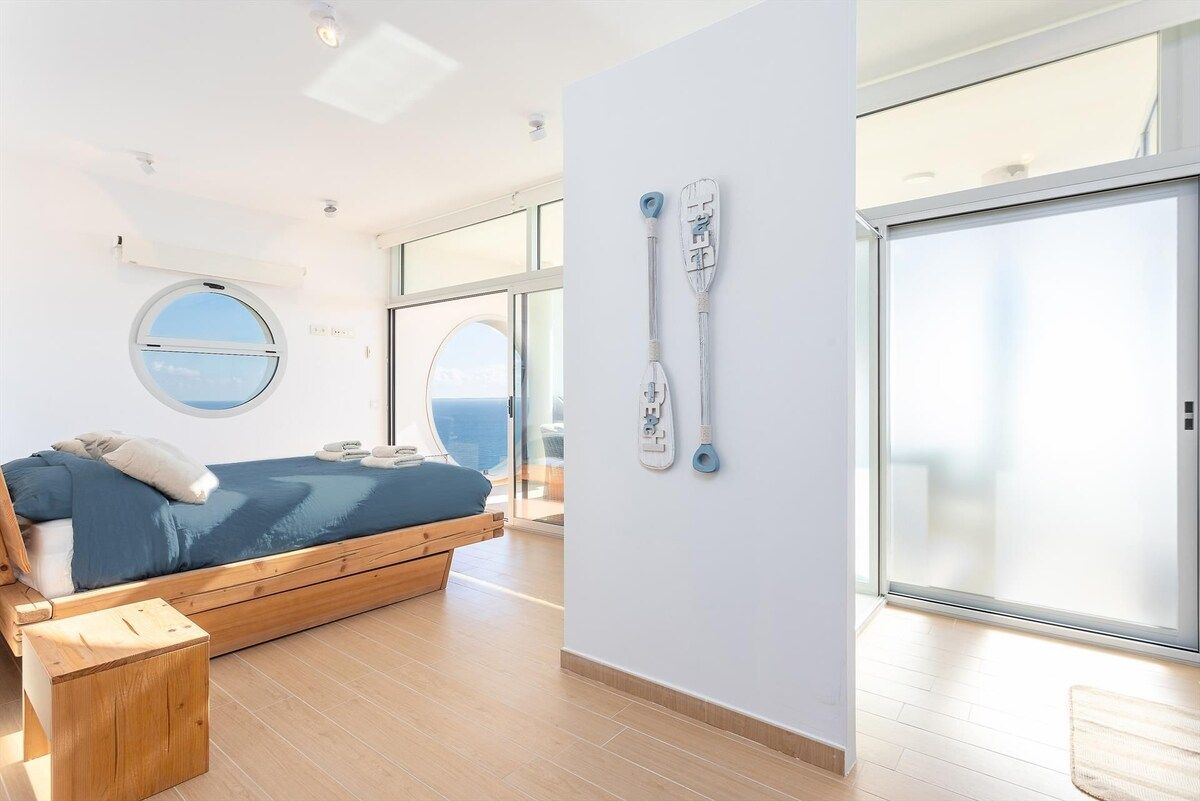 Une chambre à coucher moderne avec un lit, une fenêtre ronde et une vue sur la mer.