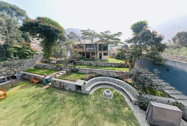 Une maison à deux étages avec un mur de soutènement en pierre, une pelouse et une piscine.