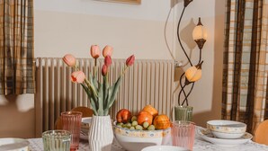 Una mesa de comedor con cuencos de estampado floral, un florero con tulipanes y un frutero con fruta.