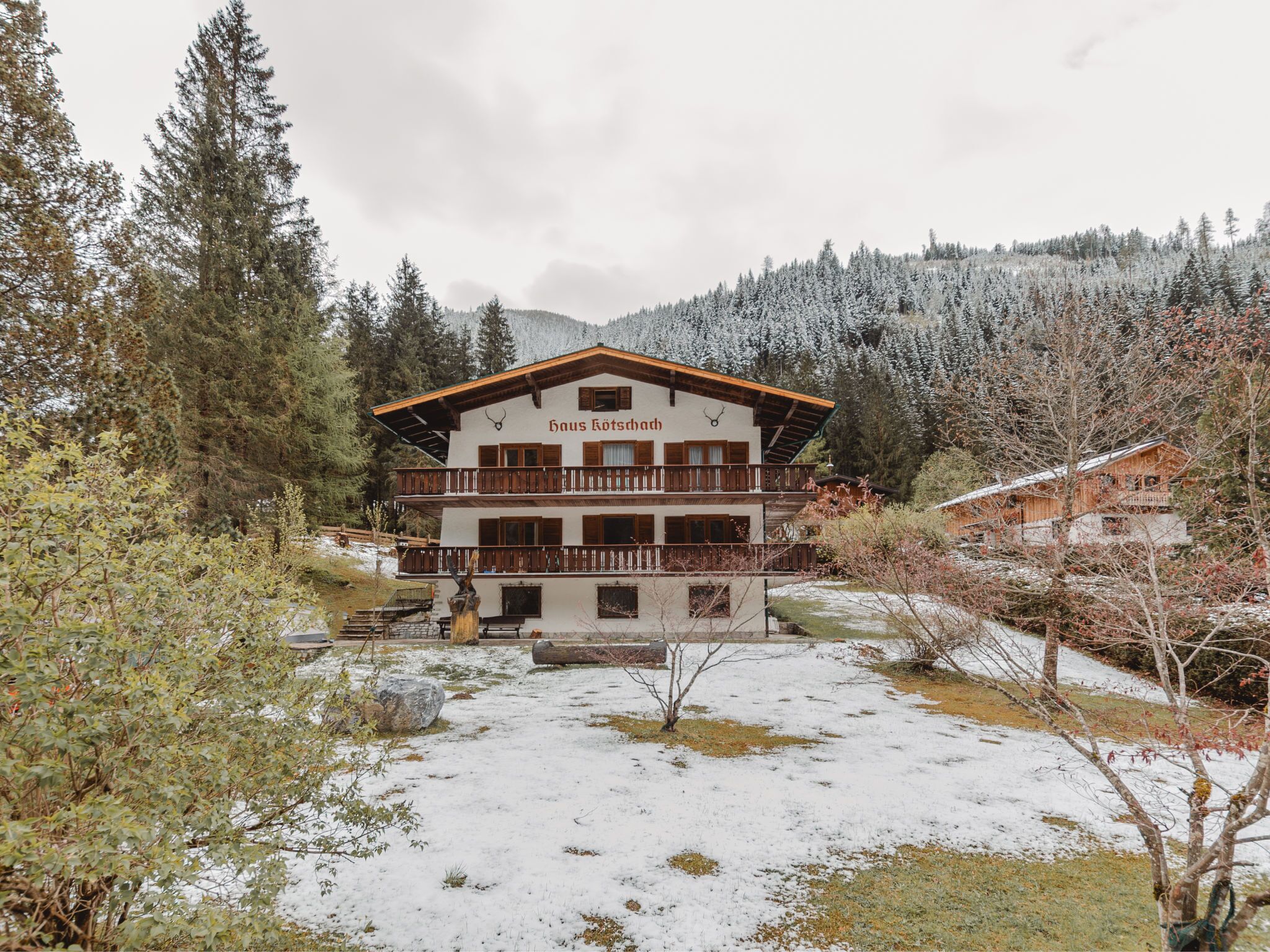 A multi-story building with a balcony, surrounded by snow-covered trees and a mountainous backdrop.