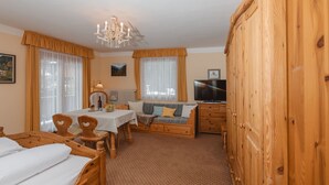 A cozy room with a wooden bed, a wooden sofa, a dining table with chairs, a chandelier, and a television. - Haus Kötschach by Interhome (Bad Gastein)