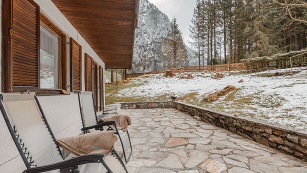 A stone-floored patio with outdoor seating, overlooking a snowy landscape and a forested mountain. - Haus Kötschach by Interhome (Bad Gastein)