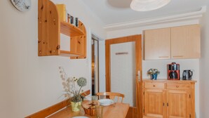 Un comedor con una mesa de madera dispuesta para dos personas, un mueble de madera con electrodomésticos de cocina y una puerta que da a otra habitación.