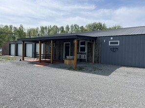 A building with a covered outdoor seating area, a gravel driveway, and a metal roof. - The Rustic Suite on Bourbon Trail (Loretto)