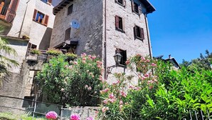 Un immeuble en pierre à plusieurs étages, doté de balcons, d’une antenne parabolique et d’un jardin où poussent des fleurs roses.