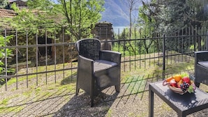 Une terrasse meublée de mobilier en osier, une table garnie de fruits et une vue sur les montagnes et un lac.
