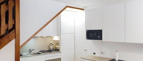 Eine kompakte Küche mit Gasherd, Backofen und Mikrowelle, einer Holztreppe und weißen Schränken.