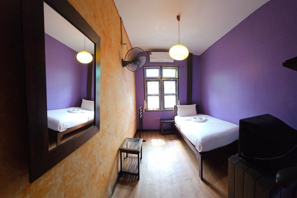 A room with two beds, a small table, a mirror, a fan, and a TV.