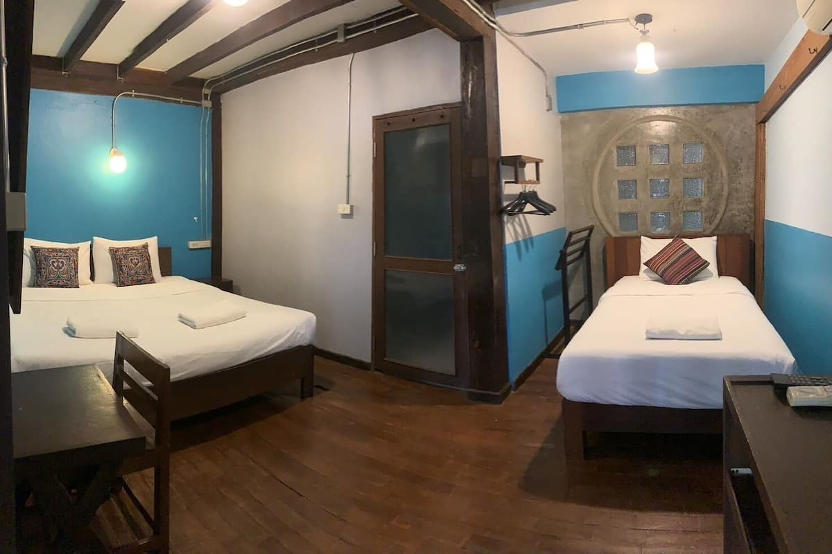 A room with two beds, wooden flooring, a door with a frosted glass panel, and a wall-mounted light fixture.