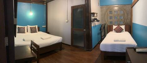 A room with two beds, wooden flooring, a door with a frosted glass panel, and a wall-mounted light fixture.