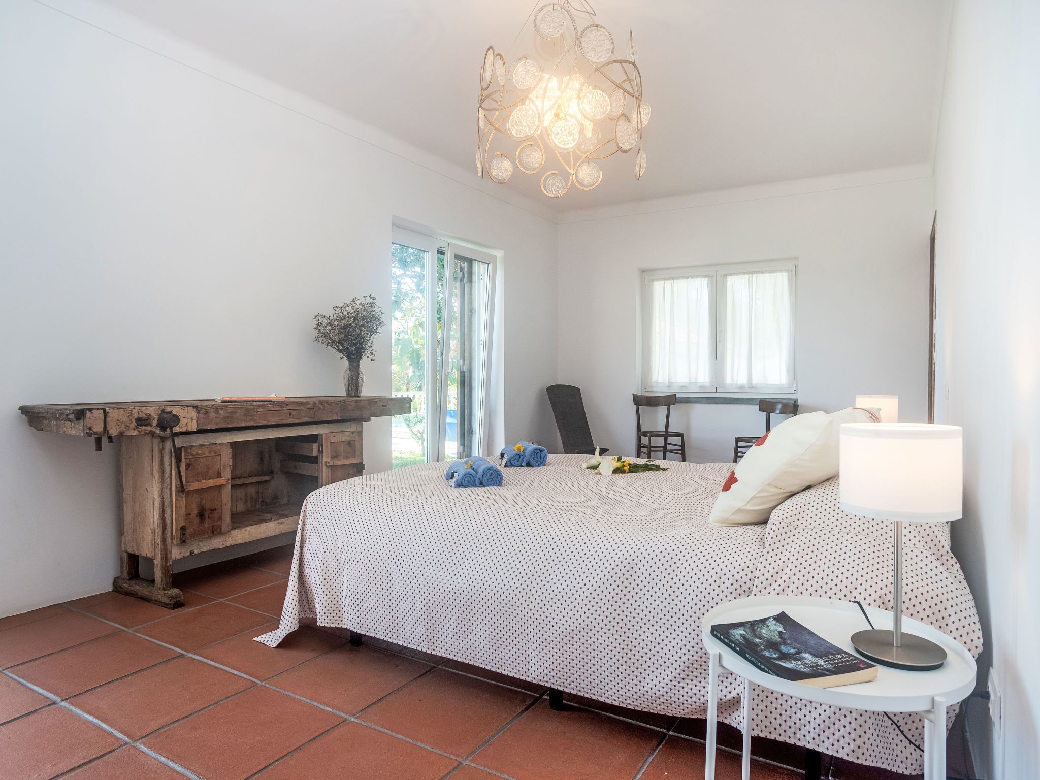 A bedroom with a bed, a desk, a chair, a lamp, and a window.