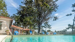 Ein Swimmingpool mit klarem, blauem Wasser, umgeben von Liegestühlen und einem Gebäude mit einem Ziegeldach.