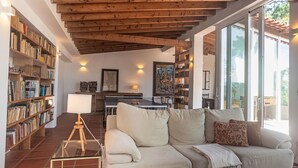 Ein geräumiges Wohnzimmer mit hohen Decken, Holzbalken, einem großen Sofa, einem Esstisch und Bücherregalen voller Bücher.