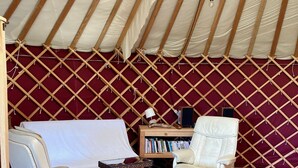 Ein gemütliches Interieur mit einem weißen Sofa, einem weißen Sessel, einem kleinen Holztisch und einem Bücherregal an einer roten Sprossenwand.