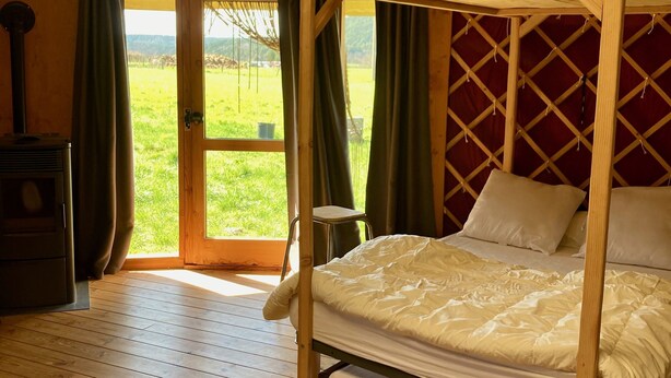 Ein gemütliches Schlafzimmer mit einem Himmelbett, Holzboden und Blick auf ein grünes Feld durch eine Tür.