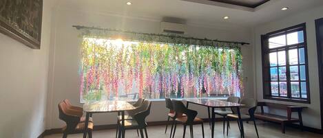 A dining area with a table and chairs, a large window with a view, and hanging plants.