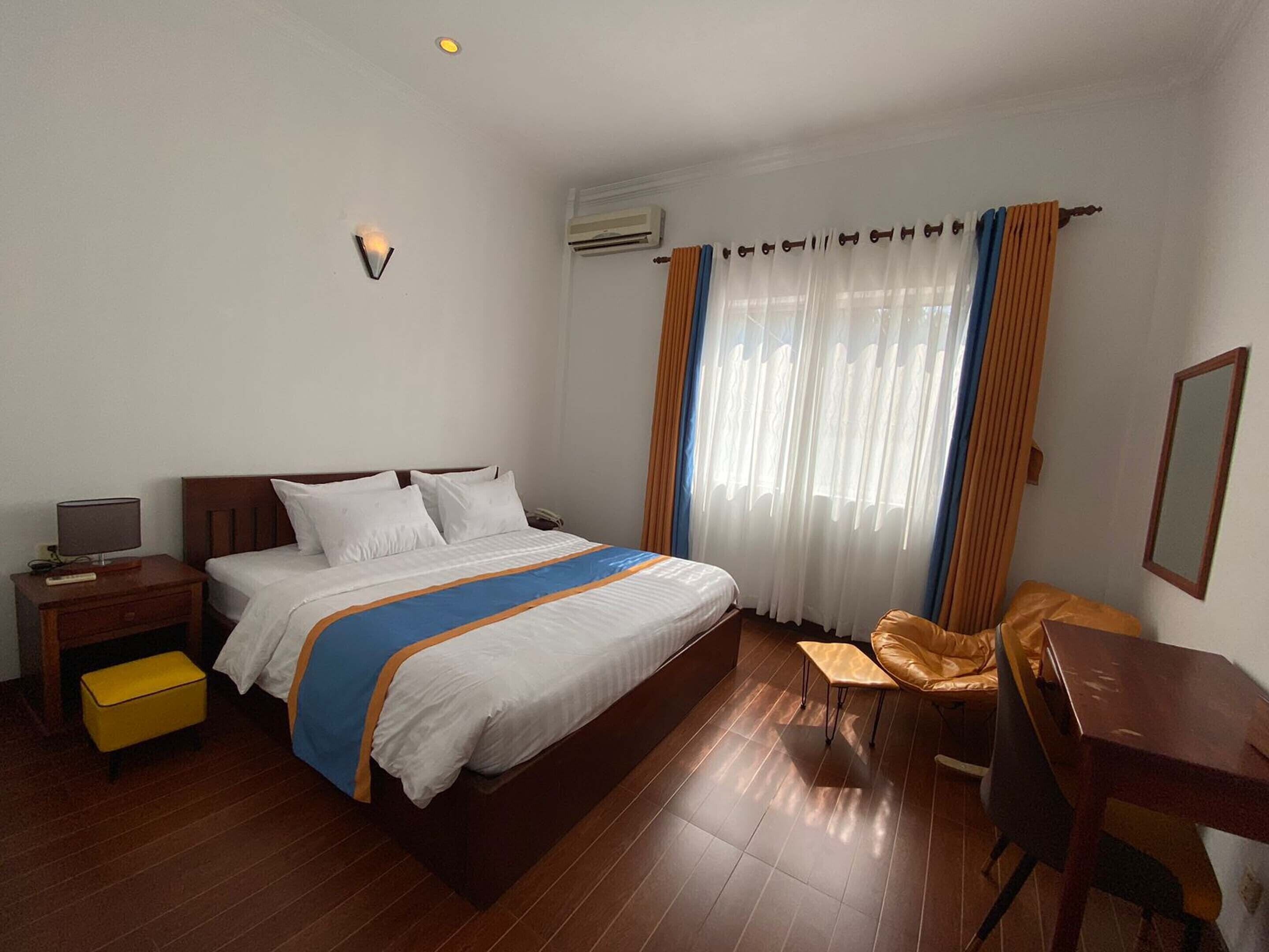 A hotel room with a bed, a desk, a chair, a nightstand, and a lamp.
