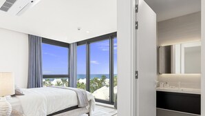 A modern bedroom with a large bed, a bathroom with a dark countertop, and a view of the ocean. - A601 (Cupecoy)