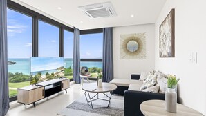 A modern living room with a large TV, a sofa, a coffee table, and a view of the ocean. - A601 (Cupecoy)