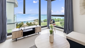 A modern living room with a large window overlooking a scenic ocean view, a minimalist sofa, a coffee table, and a TV on a wooden cabinet. - A601 (Cupecoy)