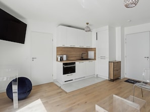 Enjoy a compact kitchen with sleek cabinetry, coffee machine, and oven, complemented by a minimalist design and a cozy seating area.