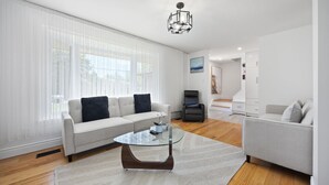 Ein modernes Wohnzimmer mit einem Glastisch, zwei Sofas, einem Sessel und einer weißen Wand mit einem Gemälde.