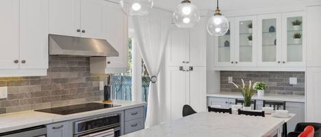 A modern kitchen with white cabinets, a marble island, and pendant lighting.