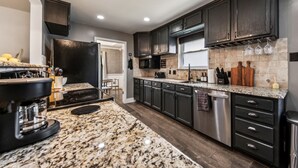 A modern kitchen with dark cabinetry, granite countertops, and stainless steel appliances. - Hot Tub/Pool/Arcade/2 Game Rooms (Lewisville)