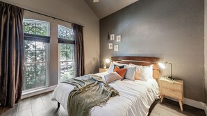 A bedroom with a large window, a bed with white linens, a bedside table with a lamp, and a wall-mounted shelf. - Hot Tub/Pool/Arcade/2 Game Rooms (Lewisville)