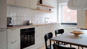 Eine moderne Küche mit weißen Schränken, einem Einbauofen, einem Toaster und einer Spüle. Ein Fenster bietet Blick auf ein Backsteingebäude.