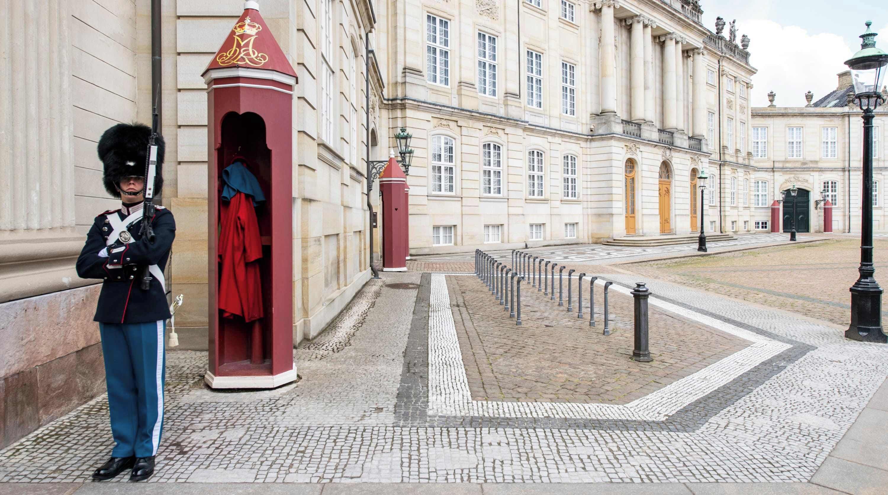 A historic building with classical architecture, a guard in uniform, and a cobblestone pathway.
