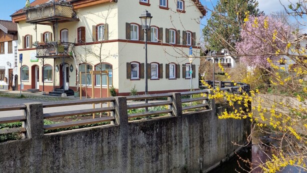 A two-story building with a balcony, a street lamp, and a small bridge over a water body.