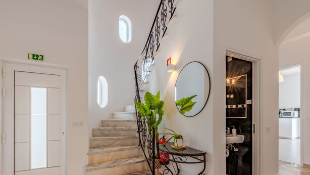 Een schoon, modern interieur met een marmeren trap, een klein tafeltje met planten, een wandspiegel en een blik op een keukenhoek.