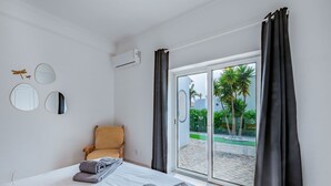 Een slaapkamer met een bed, een stoel en uitzicht op een palmboom en strand door een glazen deur.