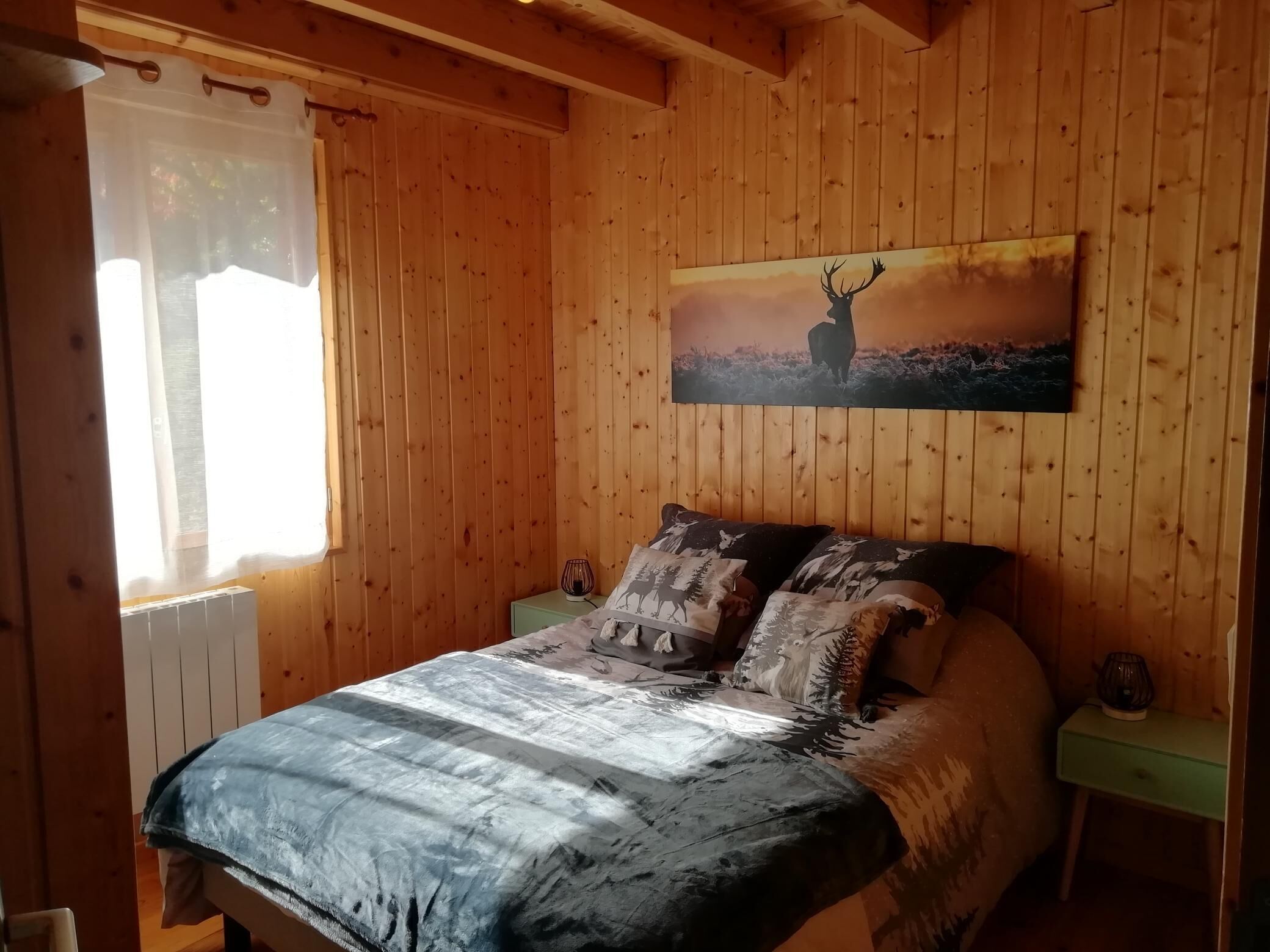A wooden-paneled room with a bed, a nightstand, a lamp, and a painting of a deer.